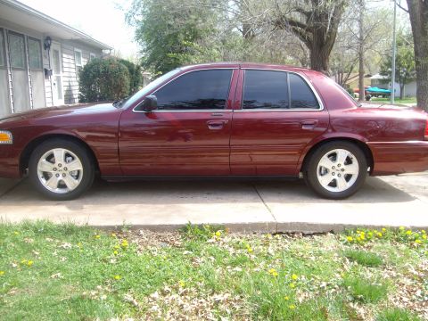 2004 Ford Crown Victoria - Full driver's-side profile of a dark red Ford Crown Victoria sedan parked on a concrete driveway, with blacked-out window tint, chrome belt…