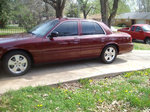 2004 Ford Crown Victoria - Driver's-side profile of a dark red Ford Crown Victoria sedan on a residential concrete driveway, showing dark tinted glass, body-color mir…