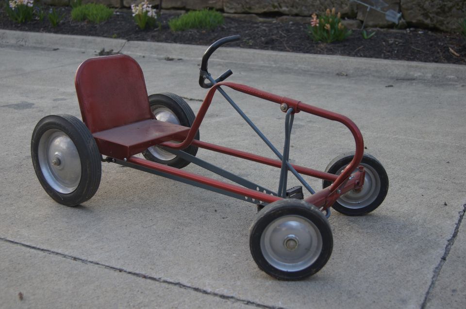 Red metal pedal car with four wheels and a black handlebar