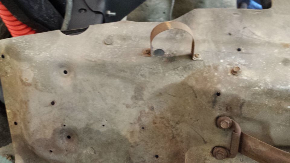 Rusty metal panel with holes and a U-shaped clamp, viewed up close