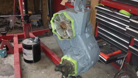 1978 Ford Bronco - A gray transfer case is prepped for painting in a workshop setting.