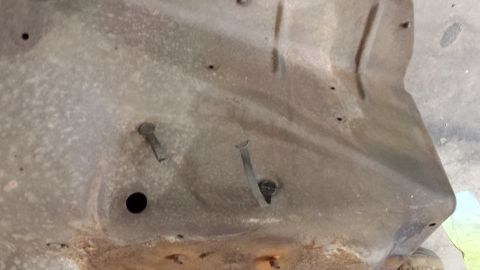 1978 Ford Bronco - The underside of a car hood shows signs of rust and wear, with several rivets and a circular opening visible.