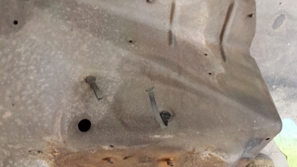 Underside of a rusty car hood with visible rivets and a black hole