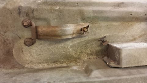 1978 Ford Bronco - Close-up view of a rusty metal bracket and bolt assembly, likely a component from a vehicle's undercarriage or engine bay.