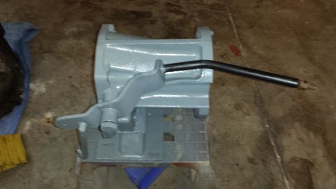 1978 Ford Bronco - A gray painted metal part with a black lever is shown on a concrete floor.
