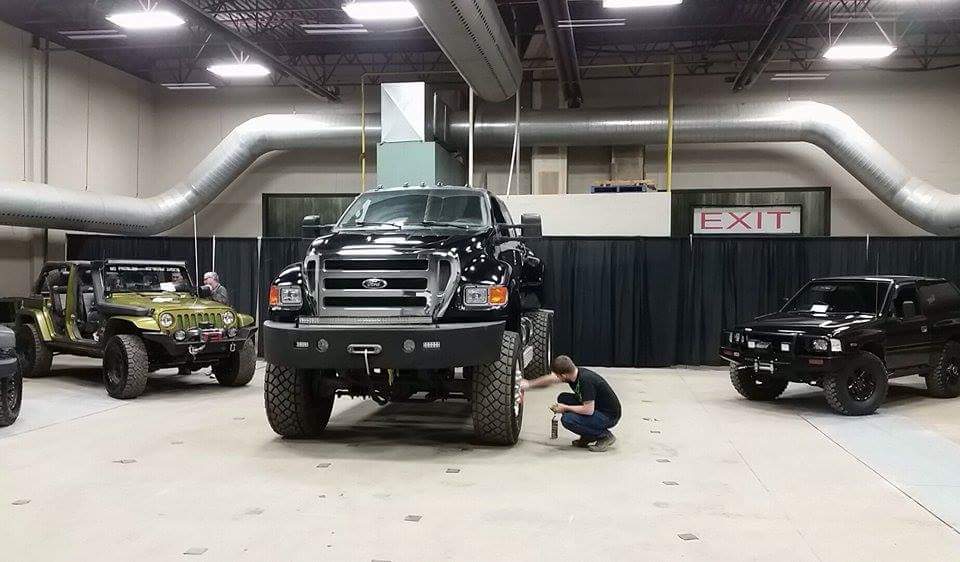 Black Ford F-650 truck with large tires, parked indoors next to a green Jeep and a black SUV