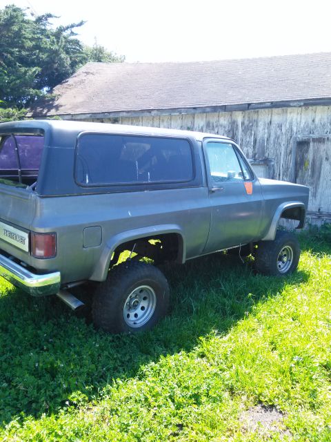 1991 Ford Bronco - This lifted Chevrolet K5 Blazer is parked on grass near a weathered wooden structure.