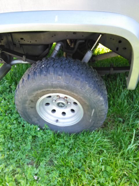 1991 Ford Bronco - Close-up view of the rear wheel and suspension system of a light-colored SUV.