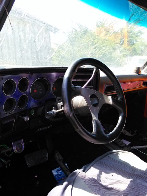 1991 Ford Bronco - The interior of a vehicle shows a steering wheel, dashboard gauges, and pedals, with a person's leg in the foreground.