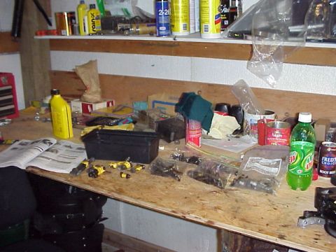 1989 Ford Bronco - A workbench is covered in various automotive parts, tools, and drinks.