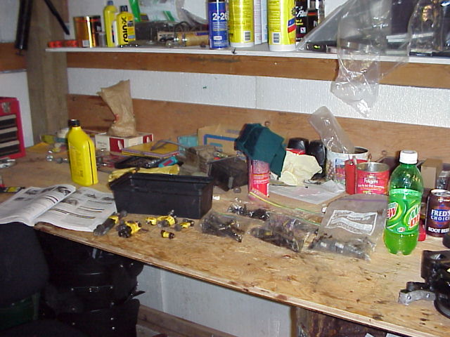Workbench cluttered with tools, parts, and beverages