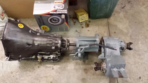 1978 Ford Bronco - A transmission and transfer case are laid out on the floor next to a box of torque converters.