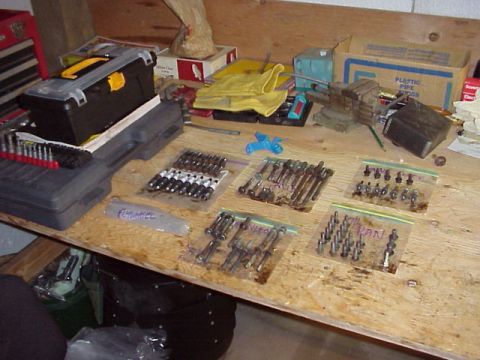 1989 Ford Bronco - A workbench displays organized hardware, including bolts sorted into bags labeled 'Valve', 'Oil Pan', and 'Fuel Injector', alongside a tool…