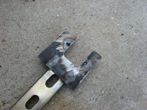 1994 Ford Bronco - Close-up of a metal bracket with visible welds and mounting holes, resting on a concrete surface.