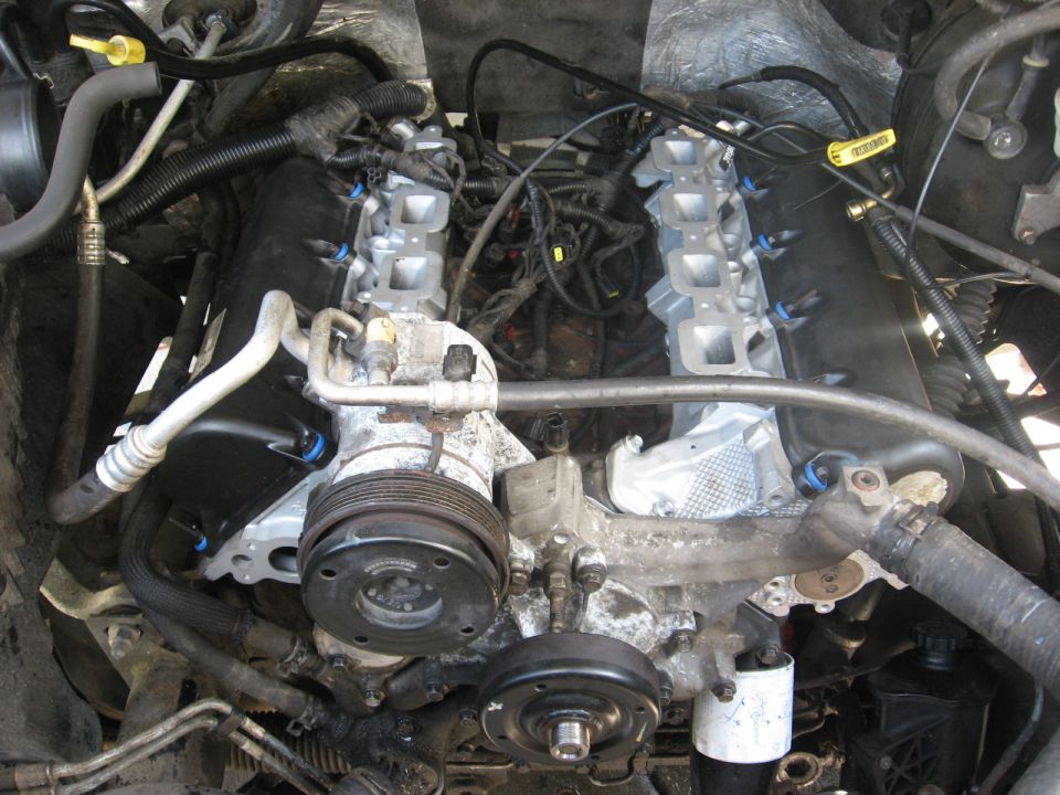Engine bay with V-engine, air conditioning compressor, and hoses visible
