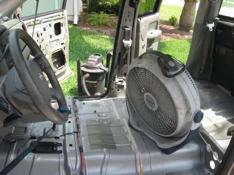 1994 Ford Bronco - The interior of a vehicle is shown with its doors removed, a fan and a shop vac on the floor.