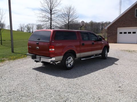 2008 Ford F-150 - A red Ford F-150 pickup truck with a camper shell is parked in front of a brick garage.