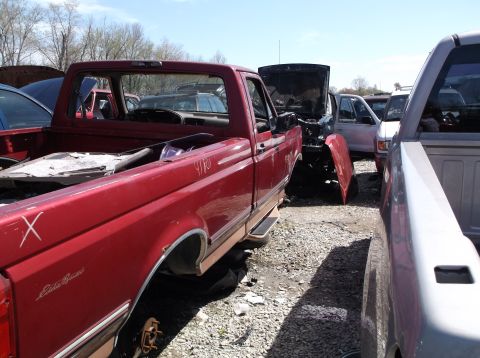 1999 Mercury Grand Marquis - Junkyard scene with a red pickup truck in the foreground and other vehicles in the background.