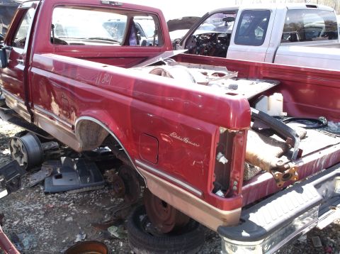1999 Mercury Grand Marquis - A red pickup truck, possibly an Eddie Bauer model, sits in a junkyard with its bed removed.