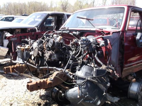 1999 Mercury Grand Marquis - Junkyard scene with a maroon truck missing its front end and engine.