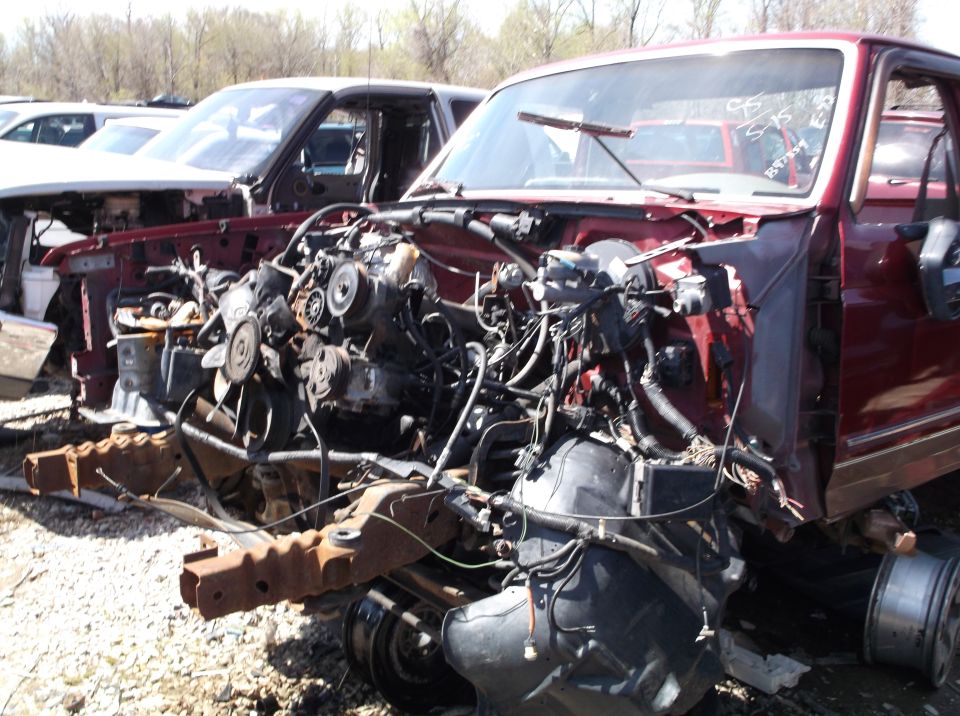 Maroon truck front end removed, engine exposed, in junkyard