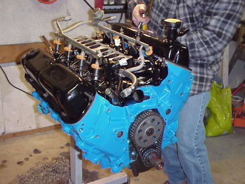 1989 Ford Bronco - Engine block assembly with fuel injection system, being worked on by a person in a workshop.