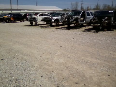 1999 Mercury Grand Marquis - Multiple vehicles stripped of parts sit in a junkyard under a clear sky.