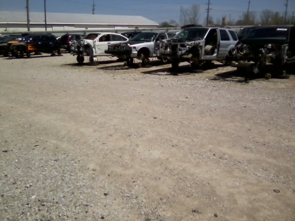 Junkyard scene with multiple stripped vehicles parked on gravel lot