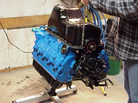 1989 Ford Bronco - A person works on a blue engine mounted on a stand.