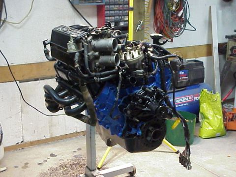 1989 Ford Bronco - Engine assembly on a stand in a workshop setting, with various tools and equipment in the background.