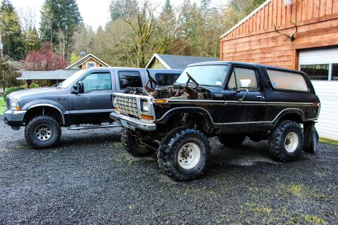 1979 Ford Bronco - Two Ford trucks, a classic Bronco and a modern Super Duty, sit parked in a gravel driveway.