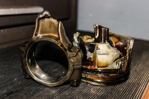 1979 Ford Bronco - Damaged engine components, including a connecting rod and a severely fractured piston, are displayed on a textured surface.