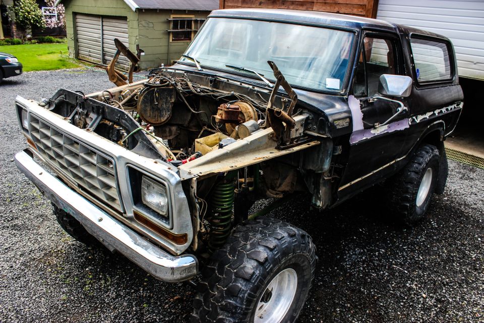 1979 Ford Bronco, front end disassembled, engine bay empty, parked on gravel
