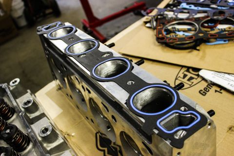 1979 Ford Bronco - Engine parts, including a cylinder head and multiple gaskets, are laid out on a workbench.