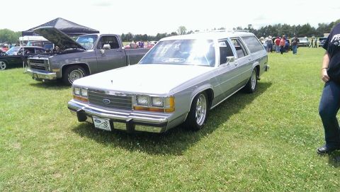2000 Mercury Grand Marquis - A silver station wagon is parked on a grassy field next to a pickup truck.