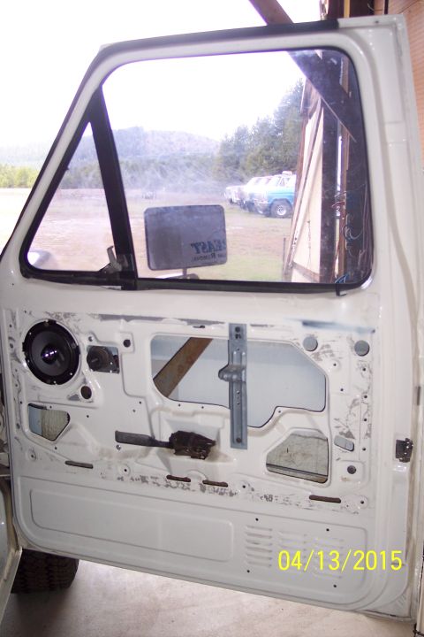1990 Ford Bronco - The interior of a white vehicle door is visible, showing the speaker and window mechanism, with other vehicles in the background.