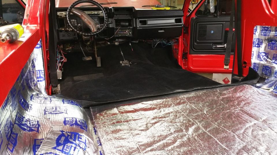 Red 1980s truck interior with black carpet and sound deadening material on the floor and door panels