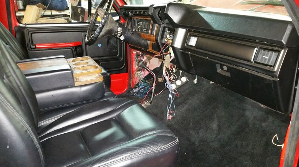 Car interior with black leather seats, exposed wires under the dashboard, and a wooden cup holder console