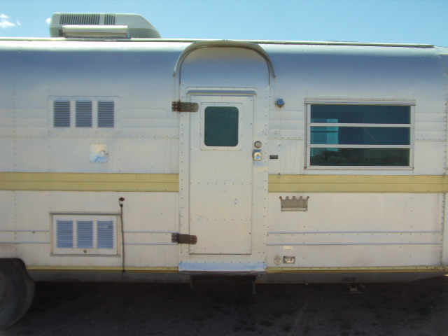 Side view of a vintage silver trailer with a yellow stripe, showing a door, windows, and air conditioner
