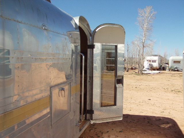 Aluminum trailer exterior with open door, showing interior reflections. Other trailers visible in background