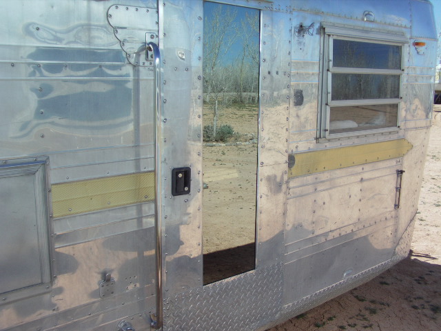 side view of an old aluminum travel trailer with a reflective door and a window
