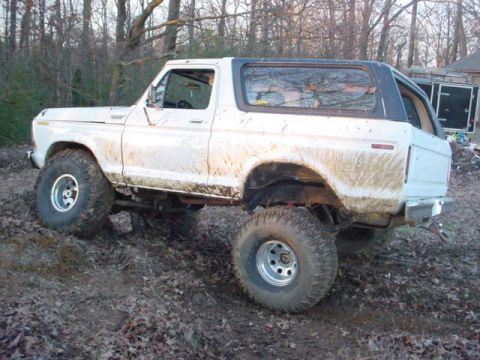 1979 Ford Bronco - Mud-covered 1978 Ford Bronco with a black top navigates an off-road trail.