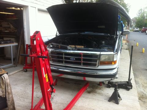 1993 Ford Bronco - Ford Bronco undergoing maintenance with hood open and engine exposed, engine hoist positioned for work.