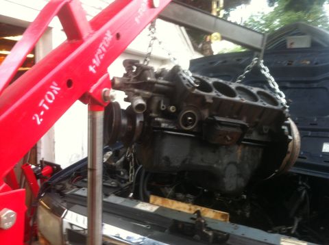 1993 Ford Bronco - An engine is suspended by chains and a red engine hoist, being removed from a vehicle.