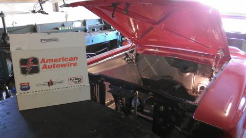 1964 Ford Fairlane - The engine bay of a red car is open, revealing a bare metal firewall and a box of American Autowire wiring for sale.