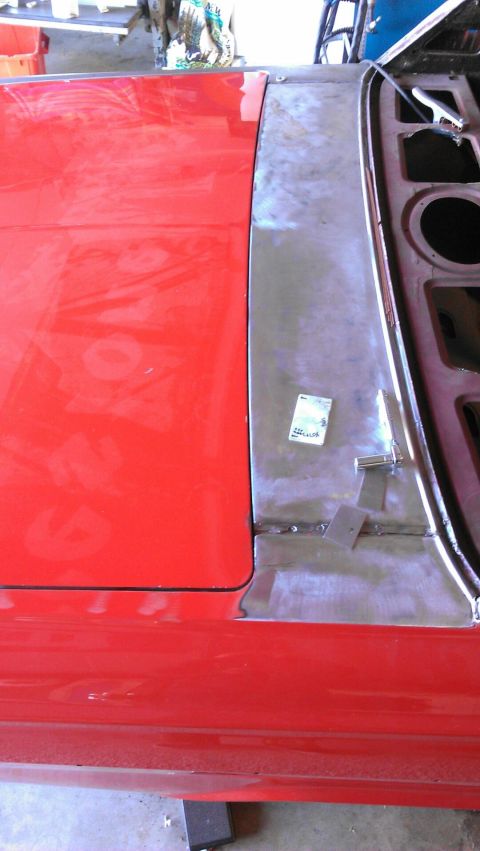 1964 Ford Fairlane - Close-up view of a red car door and a fender undergoing repair, showing unpainted metal and a small sticker on the panel.