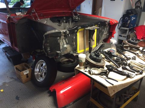 1964 Ford Fairlane - Car parts are organized on a table next to a disassembled vehicle in a garage.