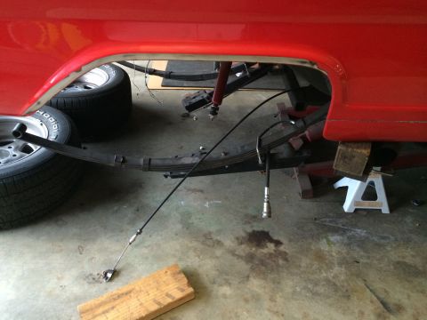 1964 Ford Fairlane - Close-up view of the rear suspension system of a red vehicle, showing leaf springs and a shock absorber.