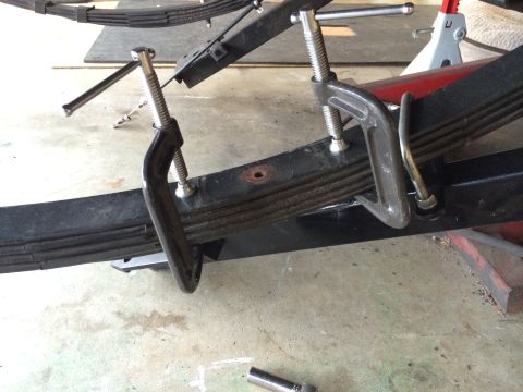 1964 Ford Fairlane - A vehicle's leaf spring is secured with C-clamps, indicating ongoing maintenance or repair work.