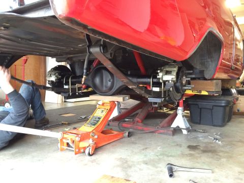 1964 Ford Fairlane - The rear suspension of a red vehicle is undergoing maintenance in a garage, with various tools and supports in place.